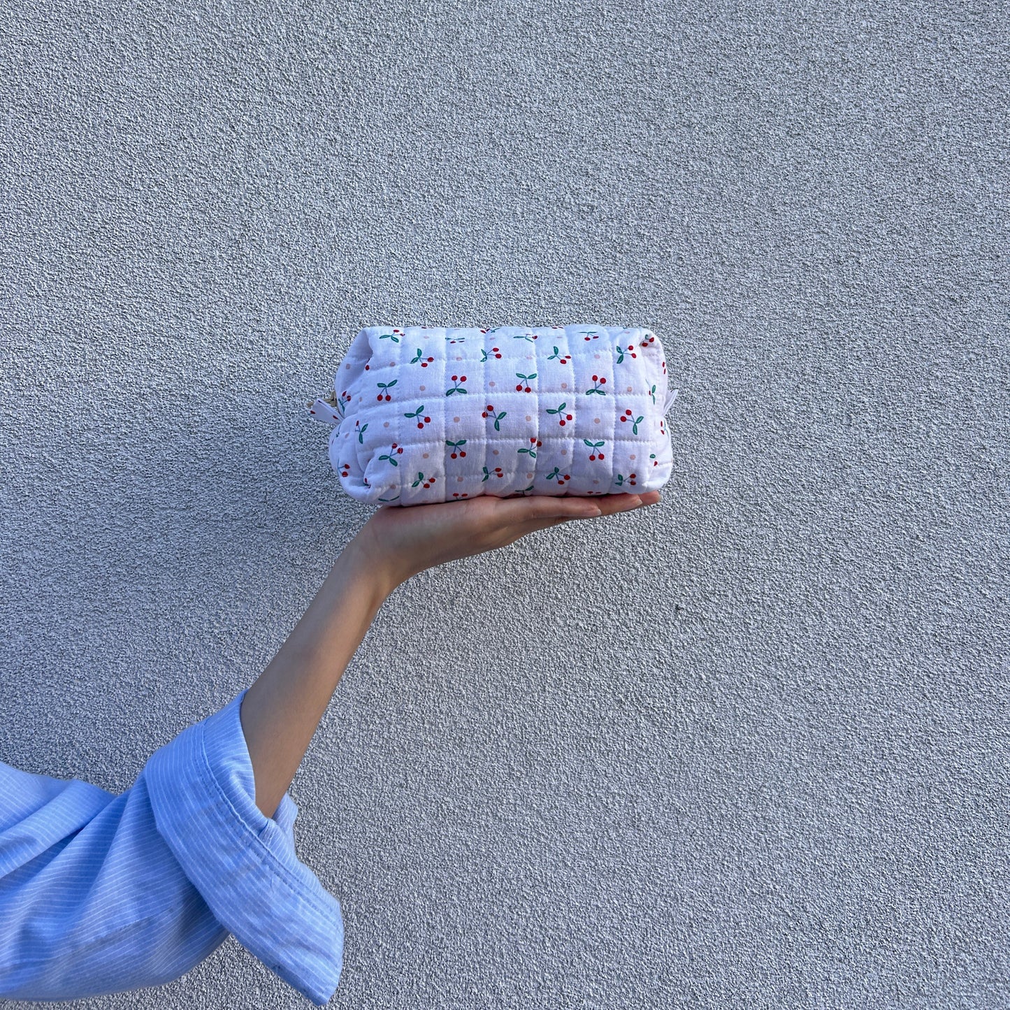 Front view of medium cherry quilted pouch held straight in hand against light gray background