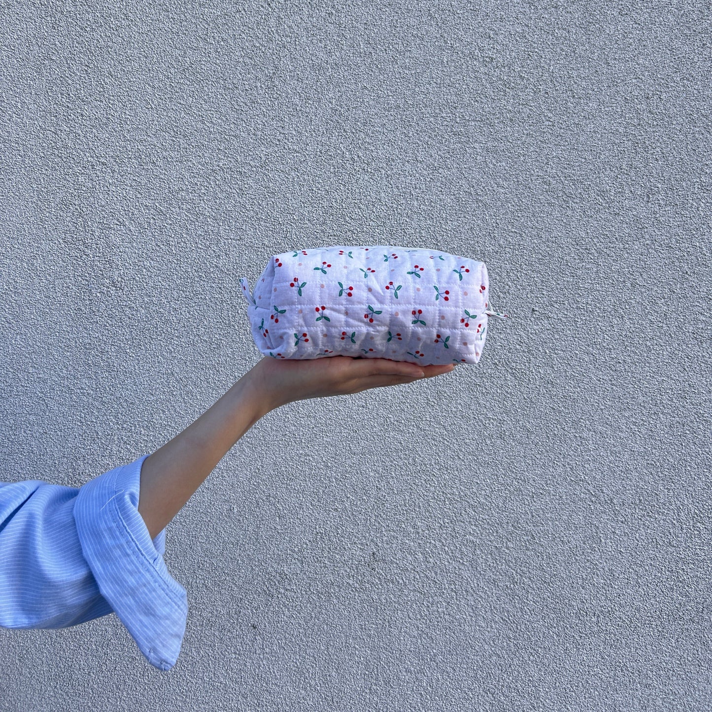 Front view of small cherry quilted pouch held straight in hand against light gray background