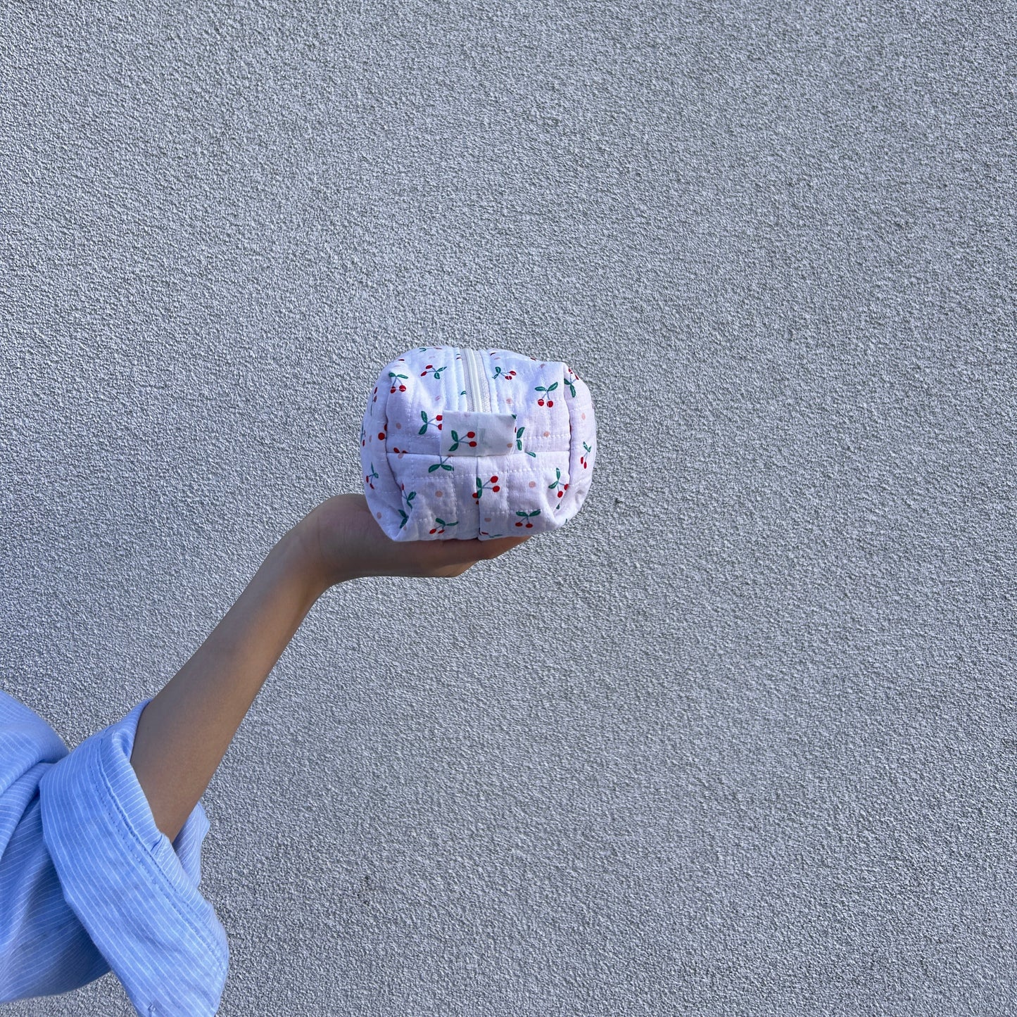 Small cherry quilted pouch held sideways in hand against light gray wall