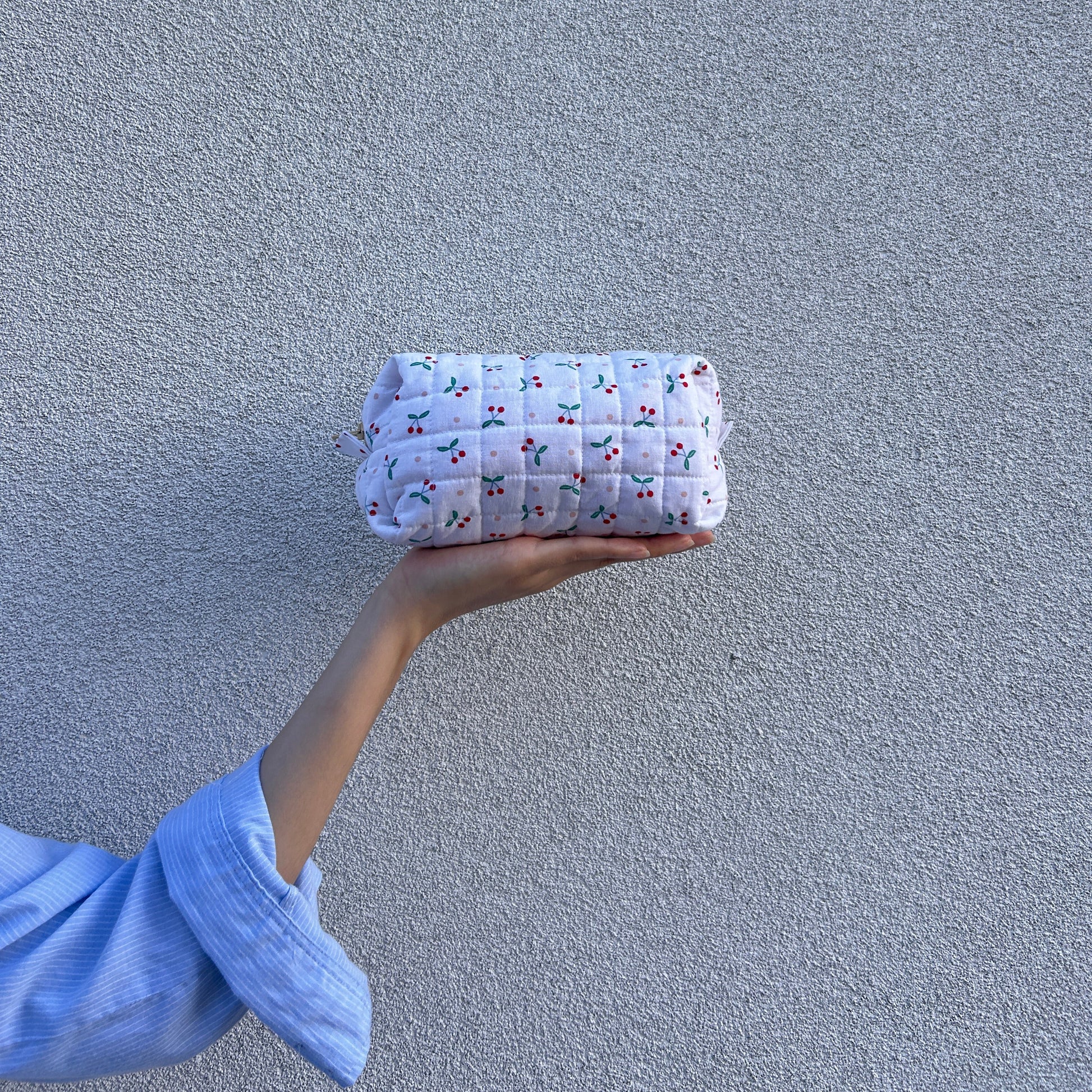 Front view of medium cherry quilted pouch held straight in hand against light gray background