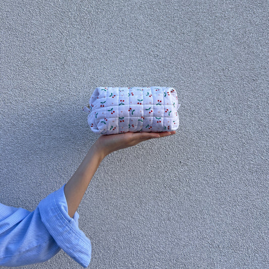 Front view of medium cherry quilted pouch held straight in hand against light gray background