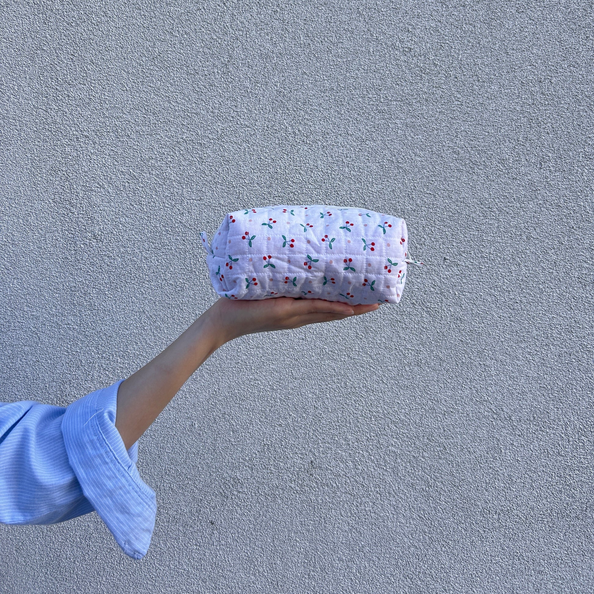Front view of small cherry quilted pouch held straight in hand against light gray background